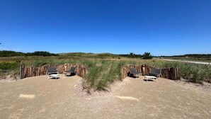A sandy beach area with two wooden fences and two lounge chairs. - Villa near Texel Beach with Sauna (De Koog)