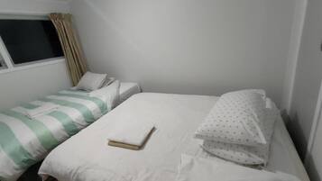 A small, single-room hotel room with two beds, one with striped bedding and the other with plain bedding.