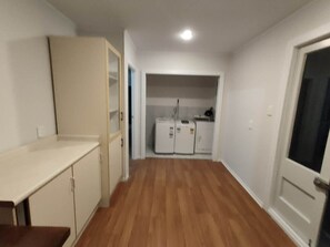 Ein Zimmer mit Holzboden, einer Küchenzeile mit Kühlschrank und Herd sowie einer Tür zu einem weiteren Zimmer.
