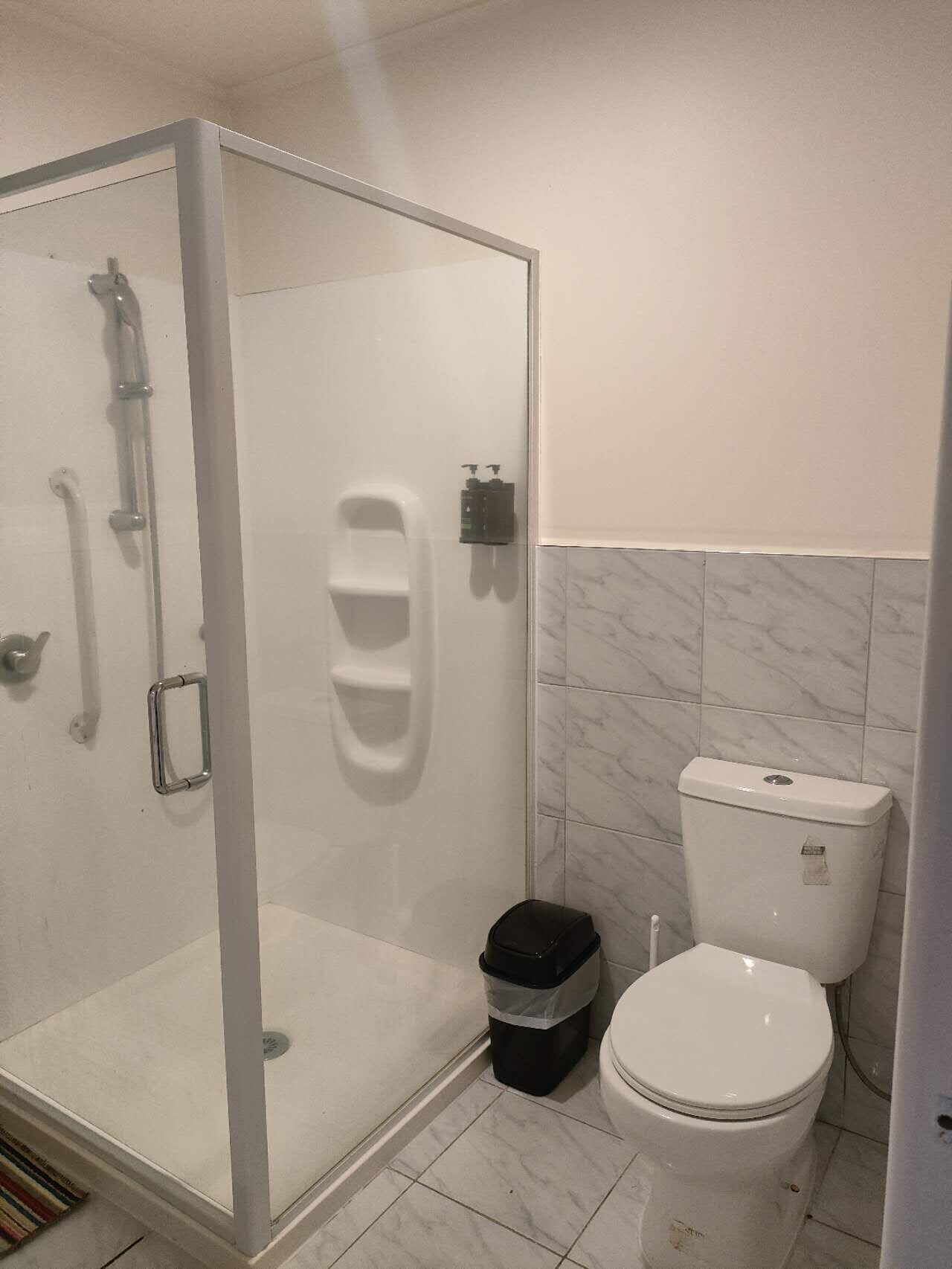 A modern bathroom with a glass-enclosed shower, a toilet, and a trash bin.