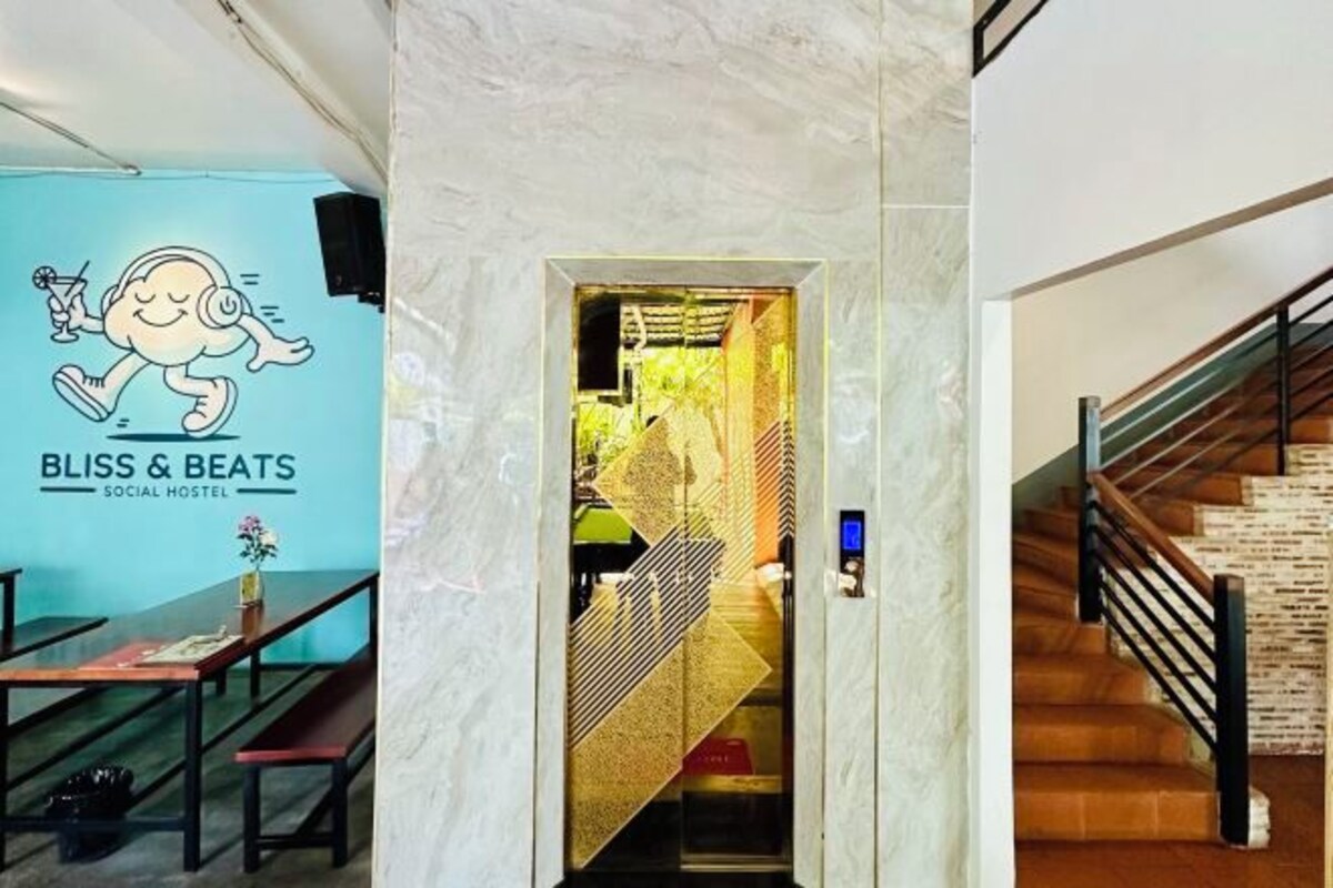 Un pasillo con pared de mármol, una escalera con detalles de madera y una puerta que da a una habitación con cortinas estampadas.