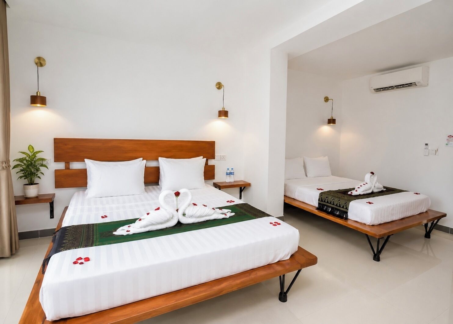 A hotel room with two beds, a wooden headboard, bedside tables, a potted plant, and an air conditioning unit.