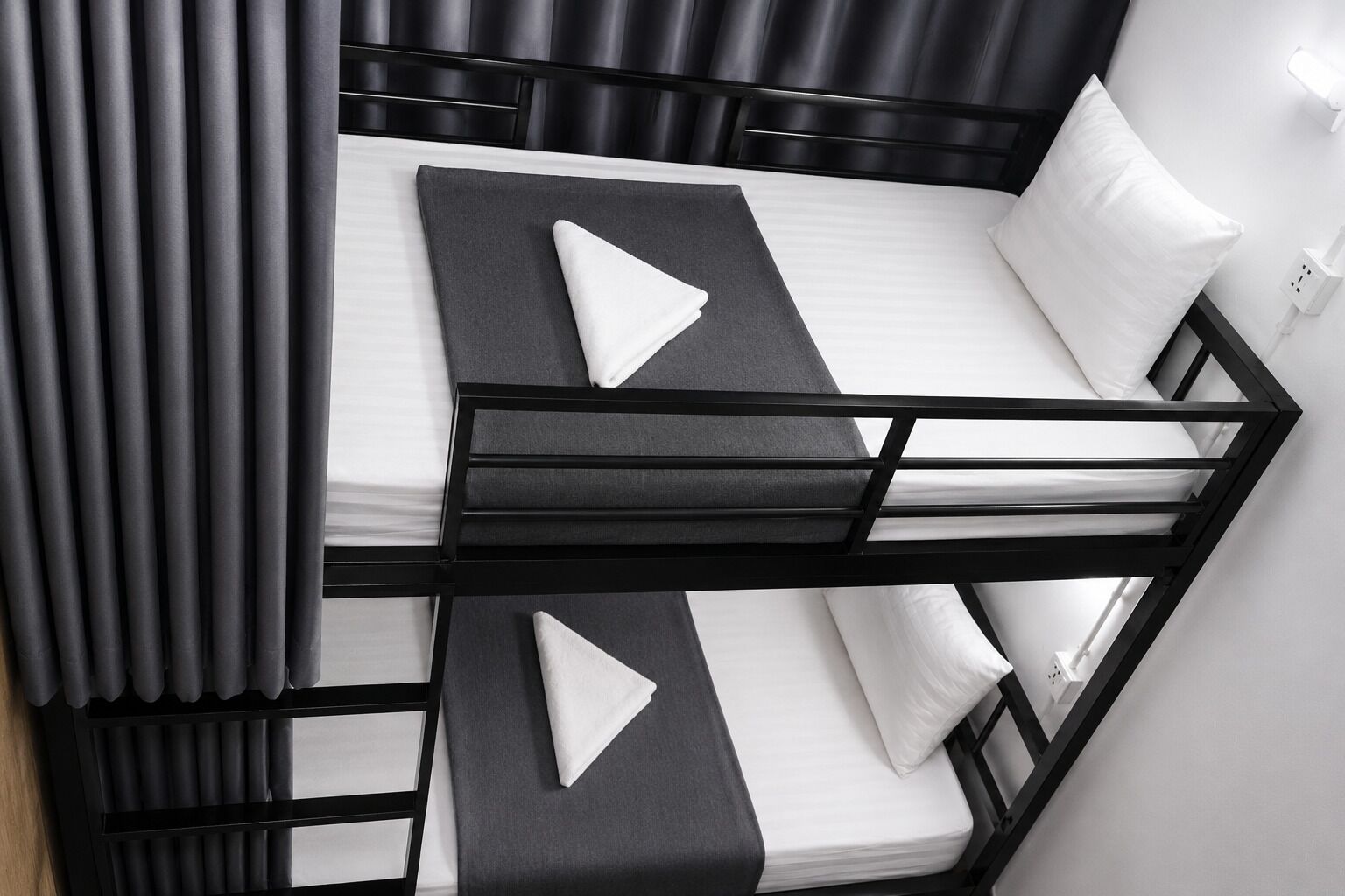 A bunk bed with a black frame, white bedding, and grey curtains.