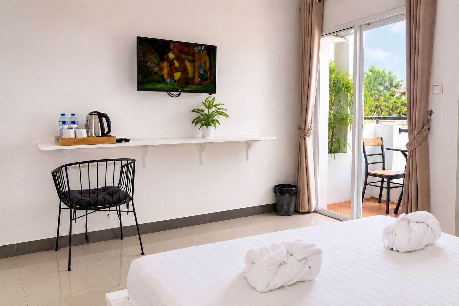 A hotel room with a bed, a TV mounted on the wall, a small table with a plant, a chair, and a balcony with a view.