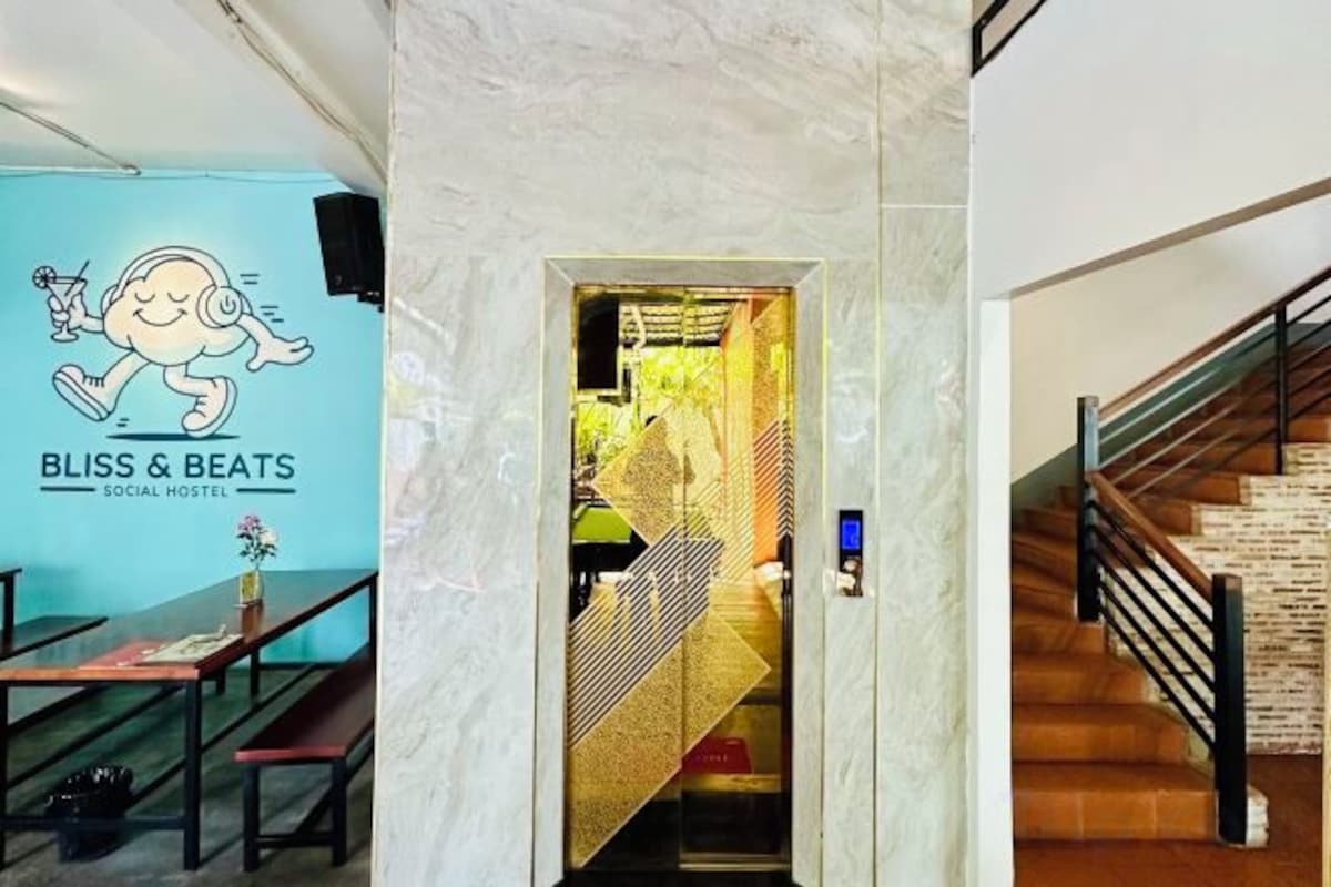 Eine Hotelhalle mit einer Marmorsäule, einer Treppe und einem Schild für 'BLISS & BEATS SOCIAL HOSTEL'.