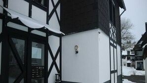 A building with a black and white facade, a door with a glass panel, and a small outdoor light fixture. - Ferienwohnung in Winterberg am Skigebiet (Winterberg)