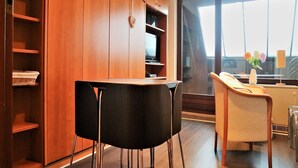 A modern room with a wooden cabinet, a dining table with black chairs, a sofa, and a large window with a view. - Ferienwohnung in Winterberg am Skigebiet (Winterberg)