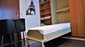 A compact room with a bed, a desk, and a bookshelf. - Ferienwohnung in Winterberg am Skigebiet (Winterberg)
