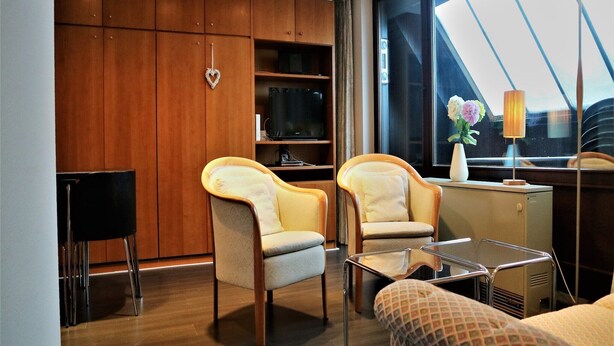 A modern living room with wooden cabinets, two armchairs, a small table, and a TV. - Ferienwohnung in Winterberg am Skigebiet (Winterberg)