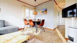 Ein modernes Wohnzimmer mit einem grauen Sofa, einem Holztisch und einem Essbereich inklusive Tisch und Stühlen.
