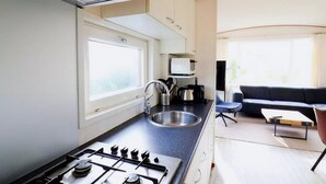 Eine kleine Küche mit einem Gasherd, einem Spülbecken und einem Fenster. Im angrenzenden Wohnbereich befindet sich ein schwarzes Sofa und ein kleiner Tisch.