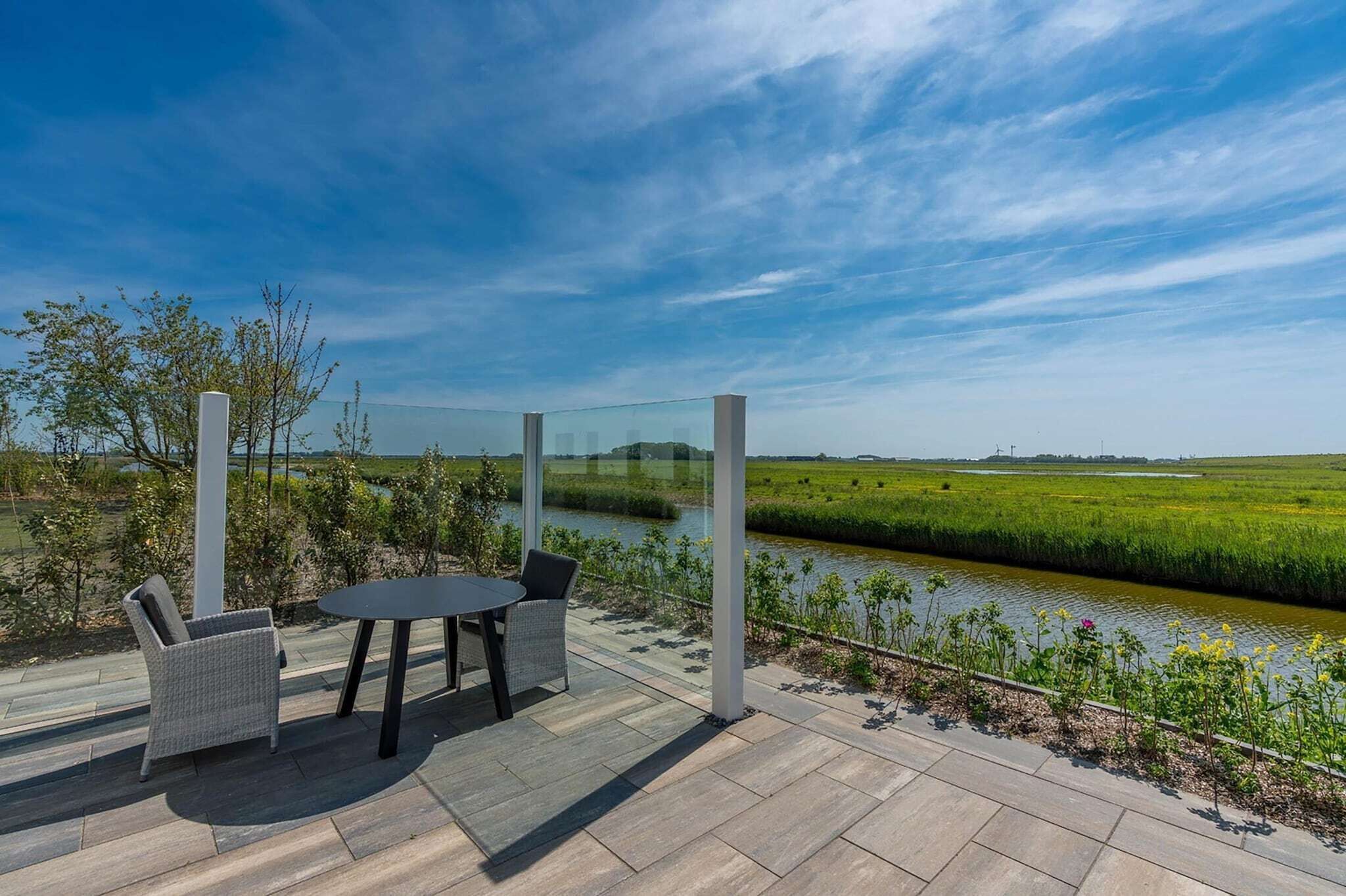 Un patio exterior con una mesa y sillas, con vistas a un río y campos.