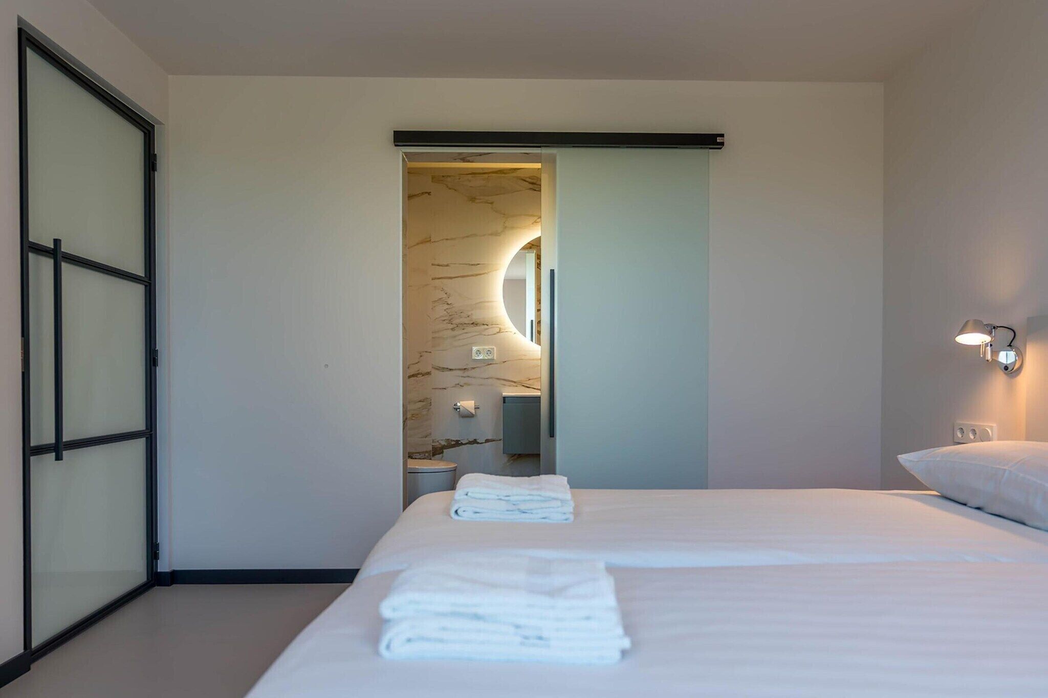 Ein modernes Hotelzimmer mit einem großen Bett, einem Badezimmer mit Marmorwand und einem Flur, der zu einem anderen Zimmer führt.