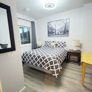 A bedroom with a bed, a bedside table, a lamp, a picture on the wall, and a window with curtains. - Cozy Country Retreat at the Baker Ranch. Pet friendly with a pet fee. Lake view. (Eagle Bay)