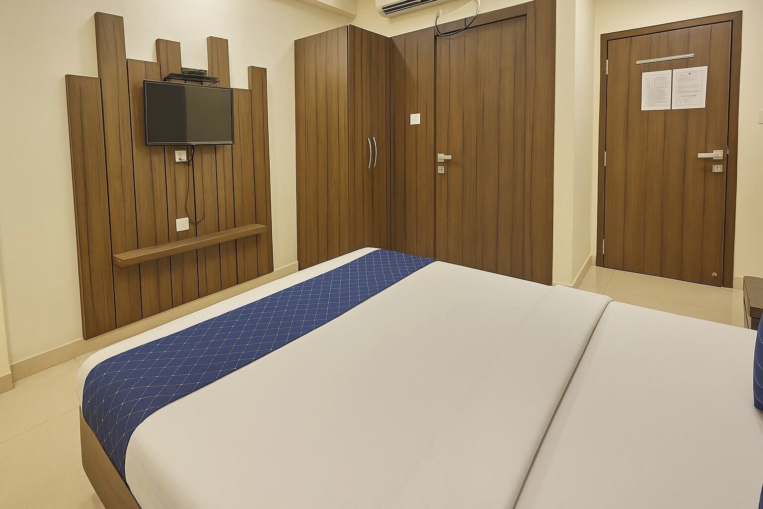 Een slaapkamer met een bed, een televisie bevestigd aan een houten paneelwand, en een garderobe met deur.