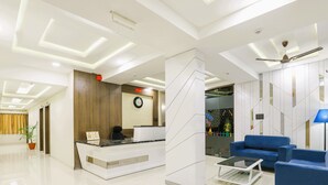 Un lobby moderno de hotel con una recepción, zona de estar y un reloj en la pared.