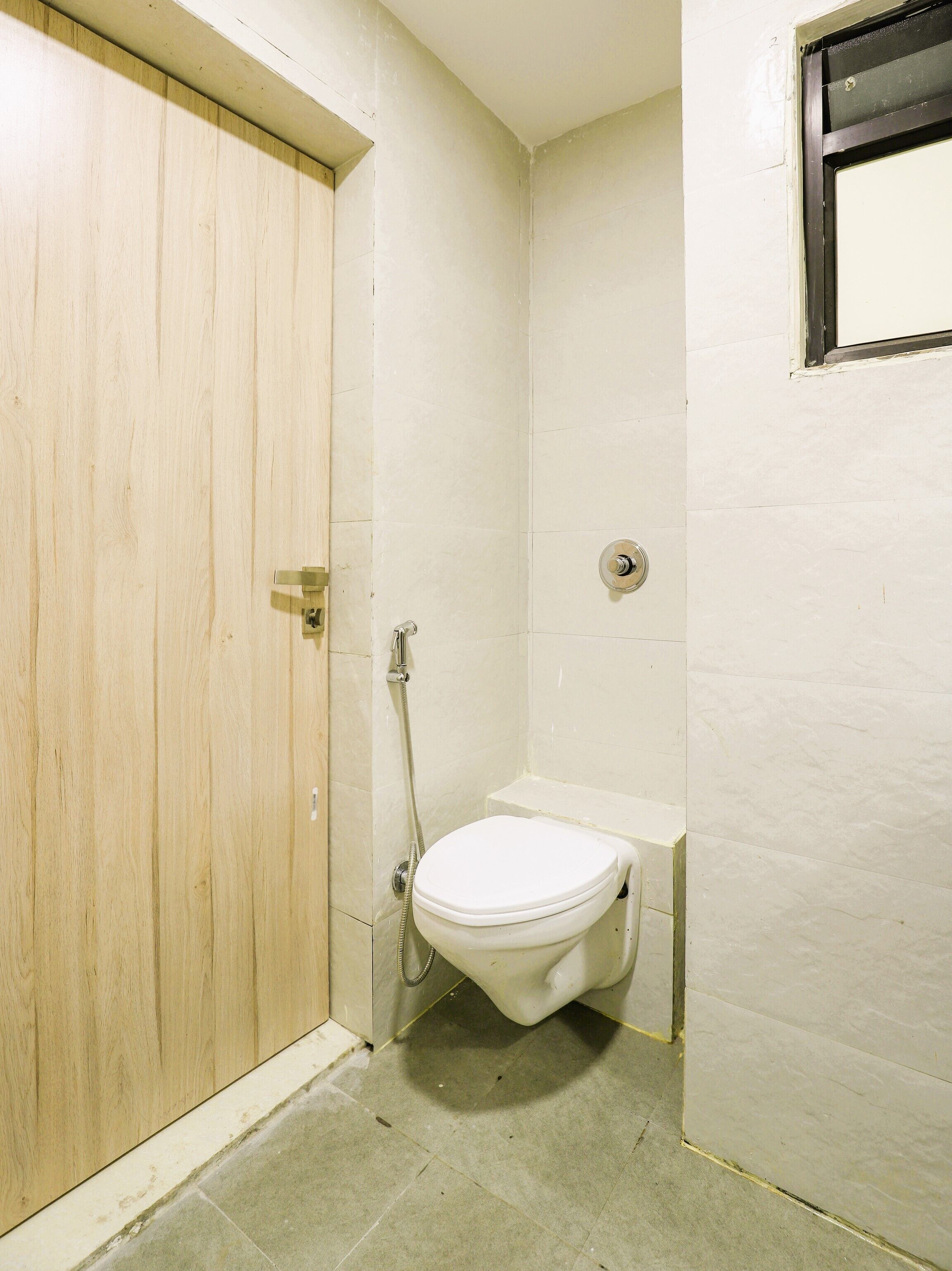 A small, compact bathroom with a wooden door, a white toilet, and a shower area.