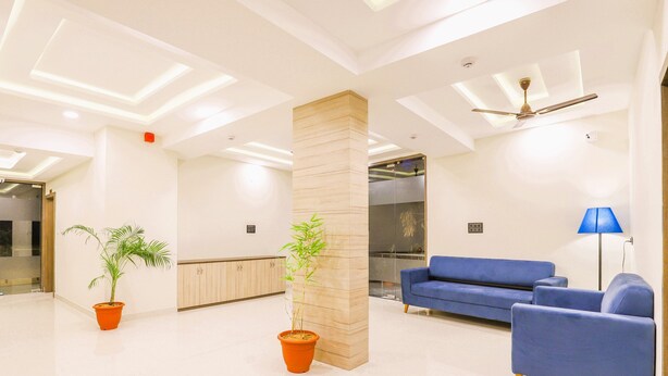 Una sala moderna con un sofá azul, dos plantas en macetas, un pilar de madera y un ventilador de techo.