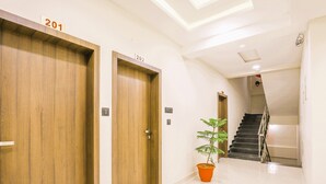 Un pasillo con dos puertas de madera identificadas con los números 201 y 202, una planta en maceta y una escalera que sube a un piso superior.