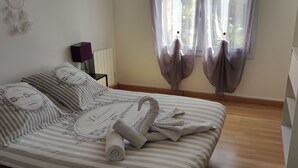 A neatly made bed with striped bedding and a rolled towel, a bedside table with a lamp, and sheer curtains on the window. - T2 45m2 quiet and close to all amenities (Lattes)