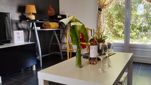 A modern living room with a white table, a yellow lamp, a framed WiFi sign, a potted plant, and a view of greenery through the window. - T2 45m2 quiet and close to all amenities (Lattes)