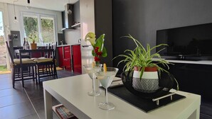 A modern living room with a white coffee table, a TV, and a dining area with red cabinets and a kitchen in the background. - T2 45m2 quiet and close to all amenities (Lattes)