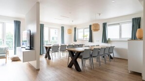 A modern dining area with a long table, multiple chairs, and a television on a cabinet.