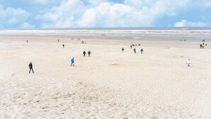 A wide sandy beach with people walking and standing, and the ocean in the background.