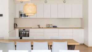 Uma cozinha moderna com armários brancos, eletrodomésticos de aço inoxidável e uma mesa de jantar de madeira com cadeiras.