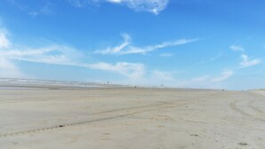 Uma praia extensa e aberta, com céu claro e horizonte distante.
