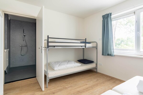 A bunk bed room with a shower, a window with curtains, and a wooden floor.