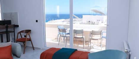 Un moderno salón con un amplio ventanal corredera que da a una terraza exterior con vistas al mar.