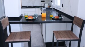 A modern kitchen with a black countertop, white cabinets, and two wooden chairs. - Duplex with terrace overlooking the sea and city, Waterfront (Monastir)