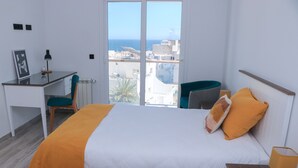 A bedroom with a bed, a desk, and a chair. There is a window with a view of buildings and the sea. - Duplex with terrace overlooking the sea and city, Waterfront (Monastir)