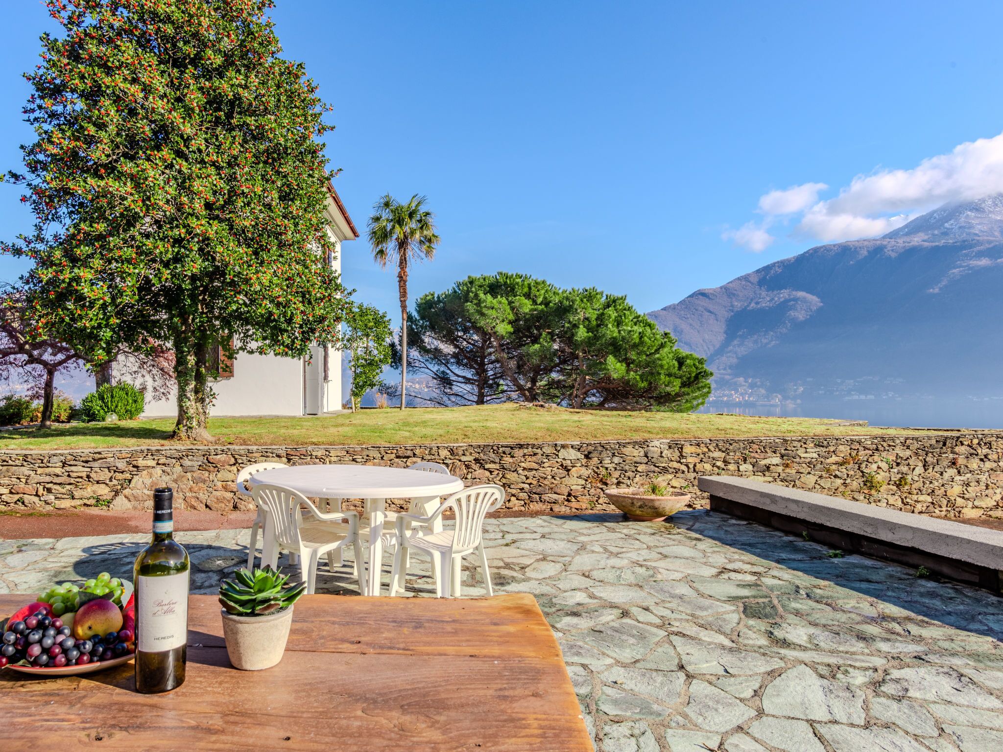 A stone patio with a table and chairs, a bottle of wine, and a plate of fruit.