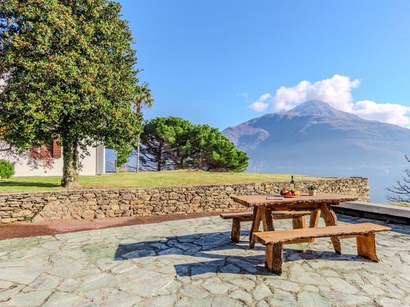 Une terrasse en pierre avec des bancs en bois et une table, d’où l’on peut admirer une montagne et un ciel dégagé.