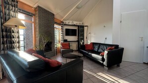 Una sala de estar con chimenea, un sofá de cuero negro, una mesa de centro redonda y un televisor montado en la pared.