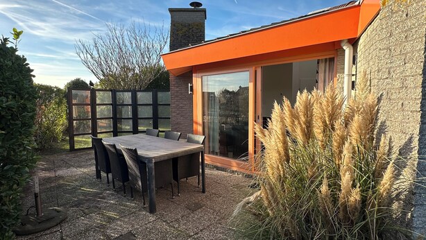 Un patio al aire libre con una mesa y sillas, un muro de piedra y un ventanal de vidrio que da a un área cubierta.