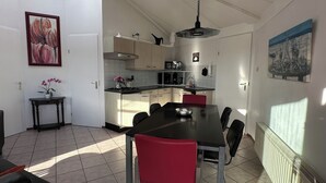 Una cocina moderna con comedor, que incluye una mesa de comedor negra, sillas rojas y una mesita auxiliar con una planta en maceta.