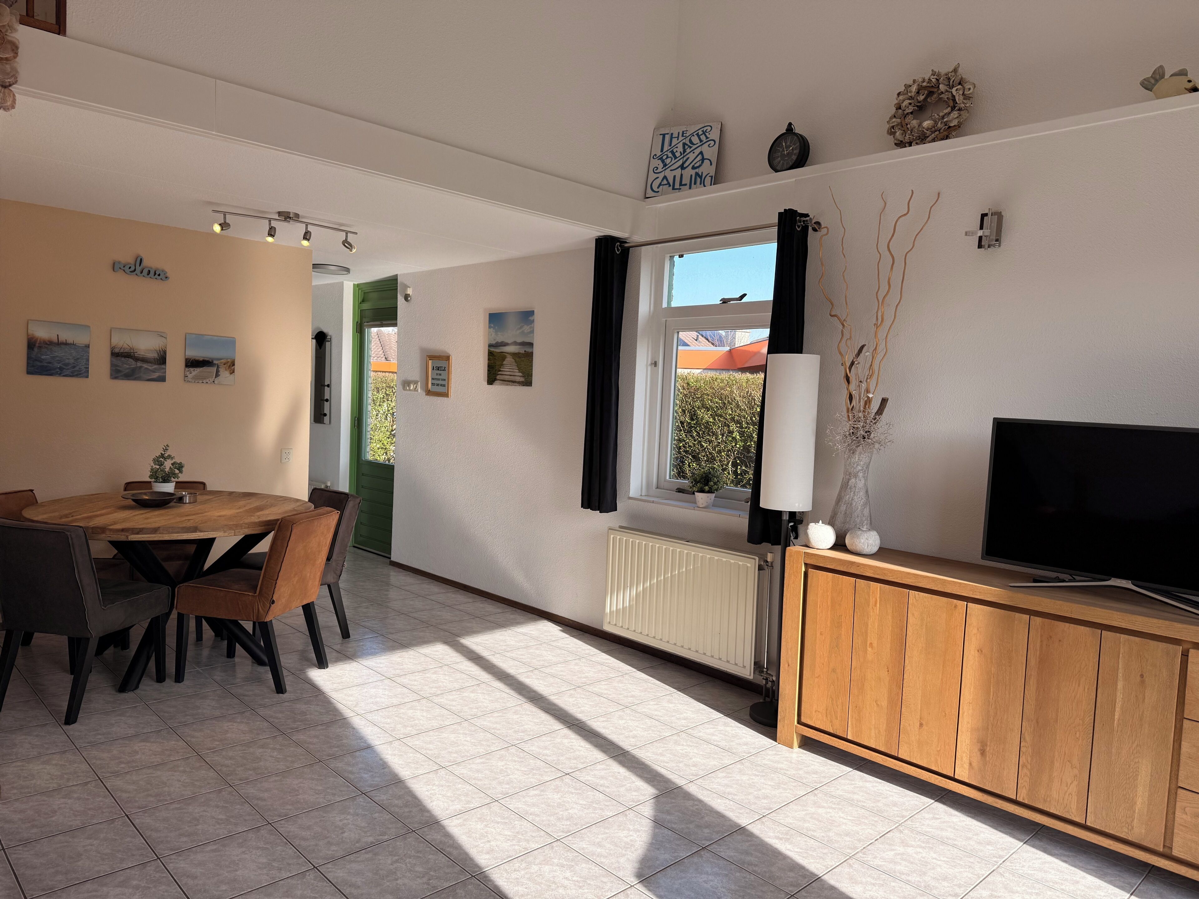 Une pièce comprenant une table à manger, des chaises, un téléviseur, une fenêtre avec des rideaux et des éléments de décoration murale.