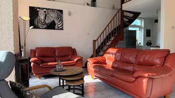 Een woonkamer met twee rode leren banken, een houten salontafel, een grijze fauteuil en een schilderij van een zebra aan de muur.