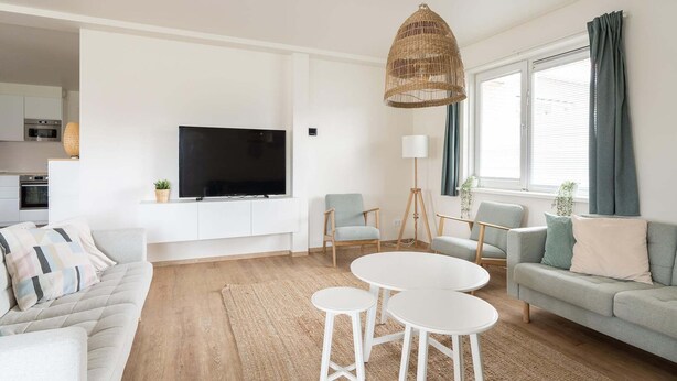 A modern living room with a flat-screen TV, two armchairs, a sofa, a coffee table, and a hanging wicker light fixture. - Group Apartment Ameland near Nes (Nes)