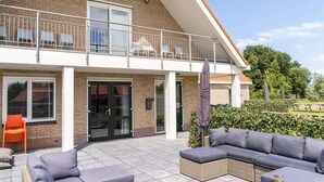A two-story house with a balcony, outdoor seating area, and a patio with a sofa and cushions. - Group Apartment Ameland near Nes (Nes)