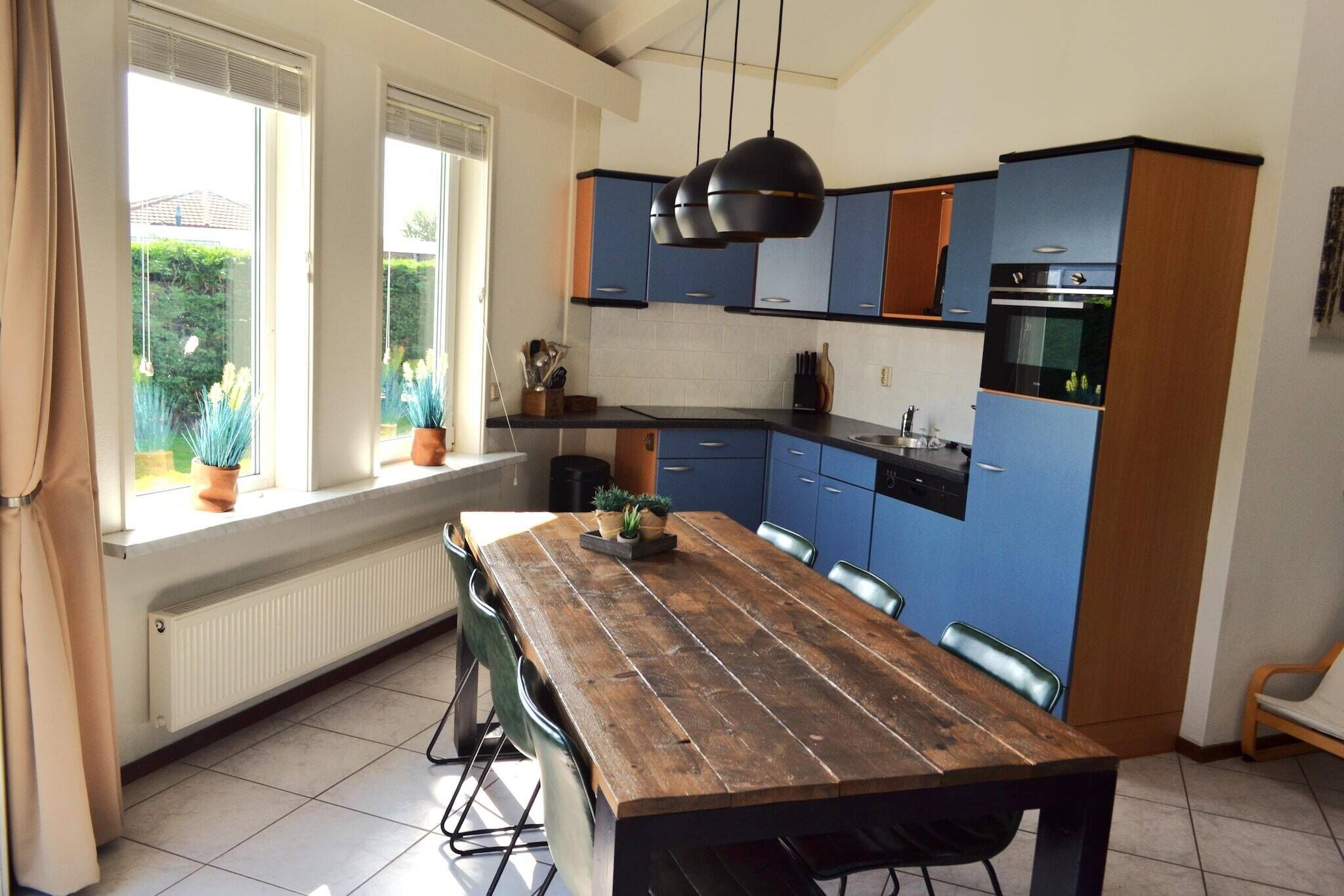 Una cocina moderna con armarios azules, una mesa de comedor de madera y vistas al jardín a través de grandes ventanales.