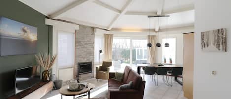 A modern living room with a sofa, TV, fireplace, and dining area with chairs and a table.