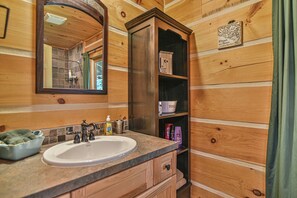 A wooden cabin bathroom with a sink, mirror, and shelves. - Bair Necessities relaxing Cabin (Old Fort)