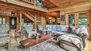 A cozy cabin interior with a wooden staircase, a large sofa, a coffee table, and a dining area. - Bair Necessities relaxing Cabin (Old Fort)