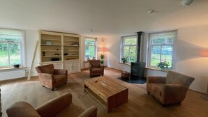 A spacious living room with a wooden coffee table, two armchairs, a bookshelf, and a fireplace. - Spacious Country Retreat (Den Burg)