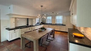 A spacious kitchen with a central island, white cabinetry, and a black countertop. - Spacious Country Retreat (Den Burg)