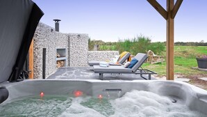 A hot tub with a wooden deck and lounge chairs, surrounded by a stone wall and a grassy field. - Holiday home near forest with wellness garden (Den Burg)